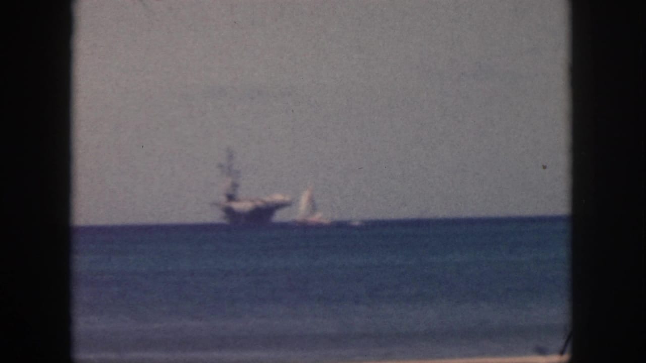 1959 Oahu 8mm frame showing a distant ship and small sailboat on the ocean under a pale hazy sky.