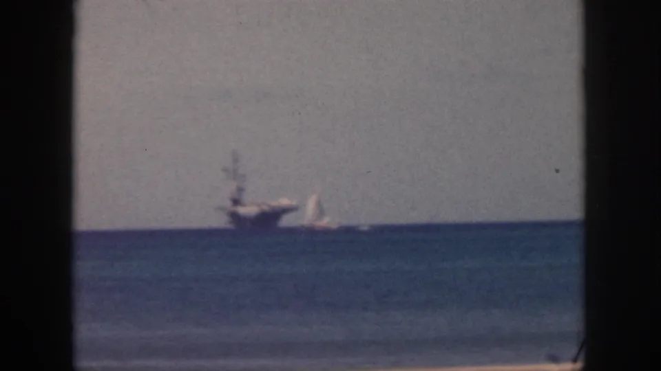 1959 Oahu 8mm frame showing a distant ship and small sailboat on the ocean under a pale hazy sky.