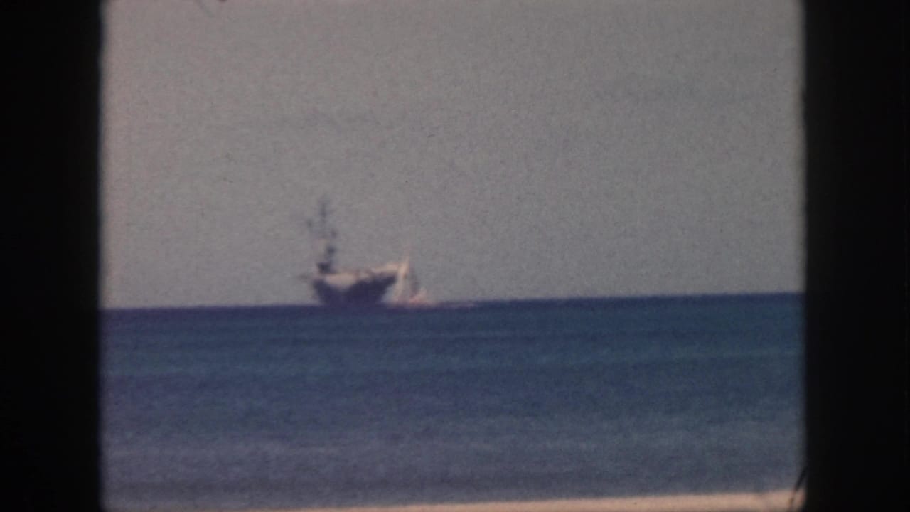 Large distant ship near a small sailboat on the ocean horizon with dark frame borders.