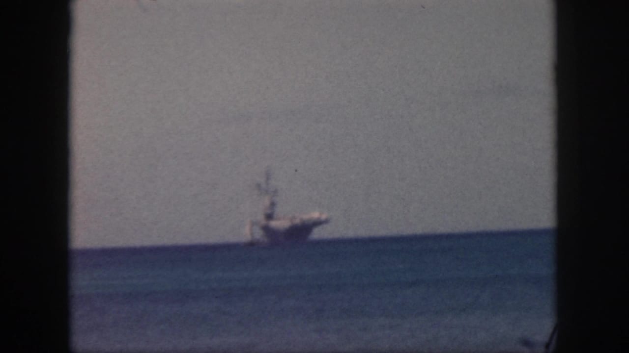 1959 Oahu 8mm frame showing a distant large ship or freighter on the ocean horizon beneath a pale sky.