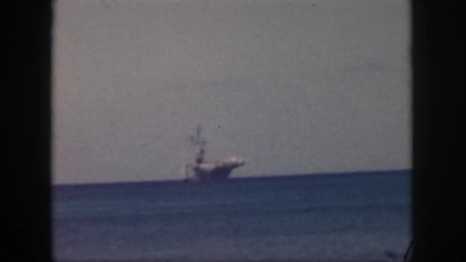 1959 Oahu 8mm frame showing a distant large ship or freighter on the ocean horizon beneath a pale sky.