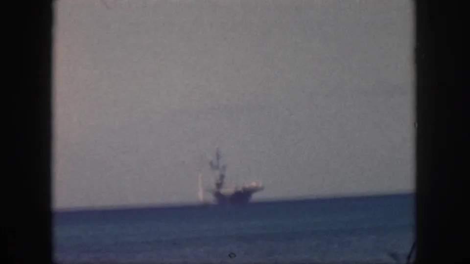 1959 Oahu home-movie frame with a distant vessel near the horizon, seen through soft grain and dark frame edges.