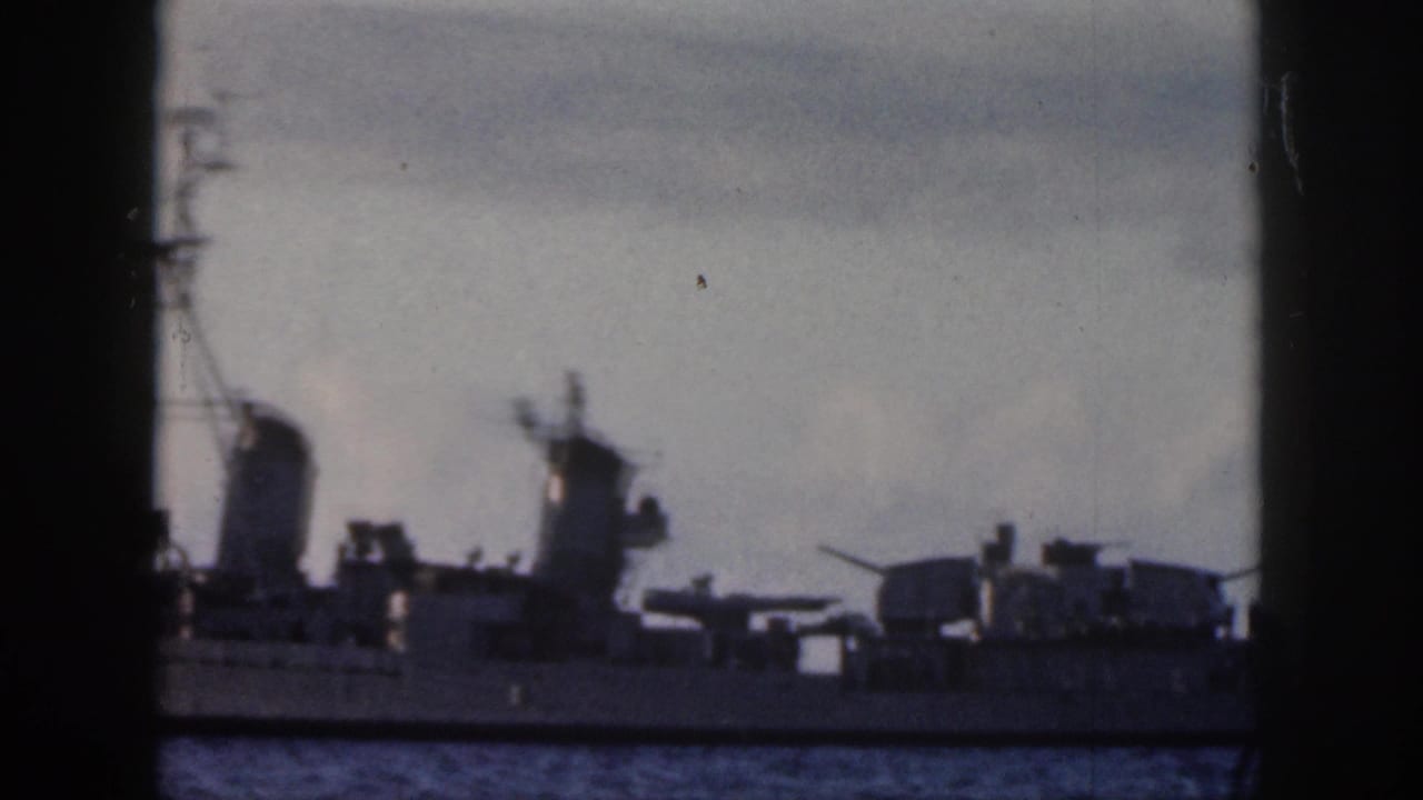 1959 Oahu 8mm frame showing a gray naval ship with turrets and stacks seen through a dark window-like foreground.