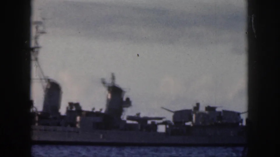 1959 Oahu 8mm frame showing a gray naval ship with turrets and stacks seen through a dark window-like foreground.