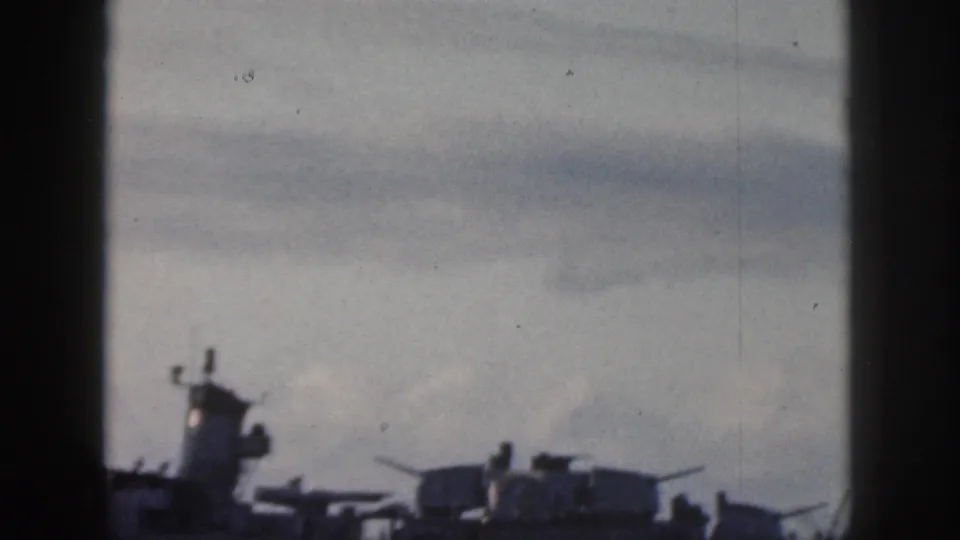 1959 Oahu home-movie still of a naval ship moving across the water, with its upper deck silhouetted against clouds.