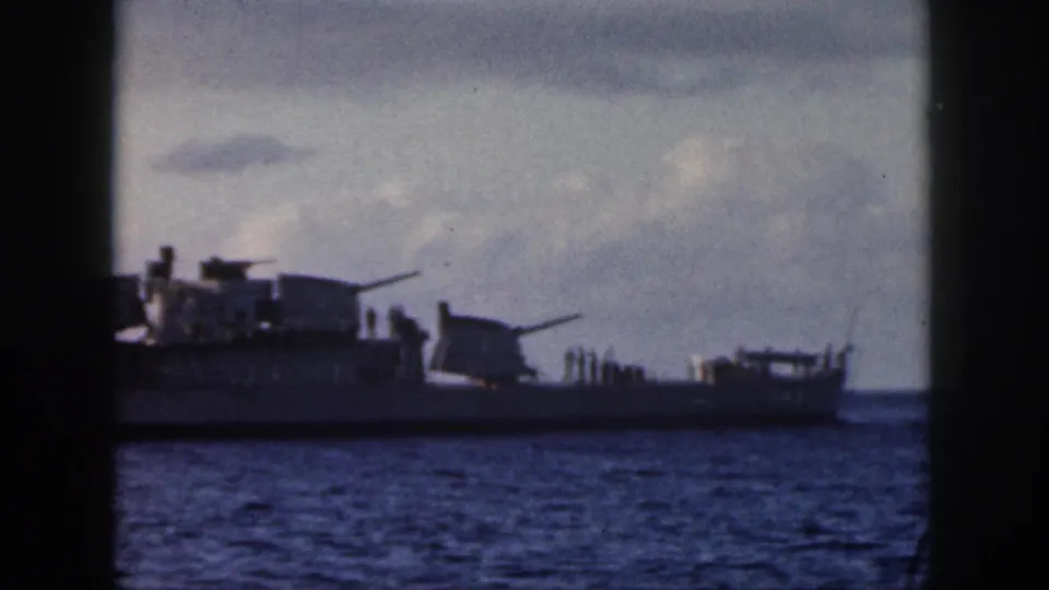 1959 Oahu 8mm still showing a side view of a naval vessel, with small deck figures and gun mounts visible above the ocean.
