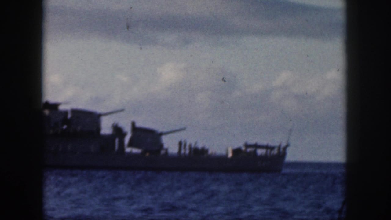 1959 Oahu 8mm frame showing a U.S. Navy warship silhouetted on calm water through dark foreground framing.