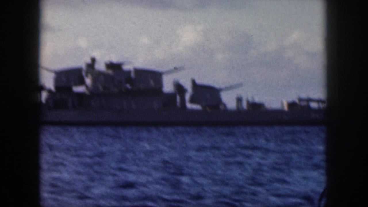 Closer view of a naval ship with deck guns and small figures on deck.