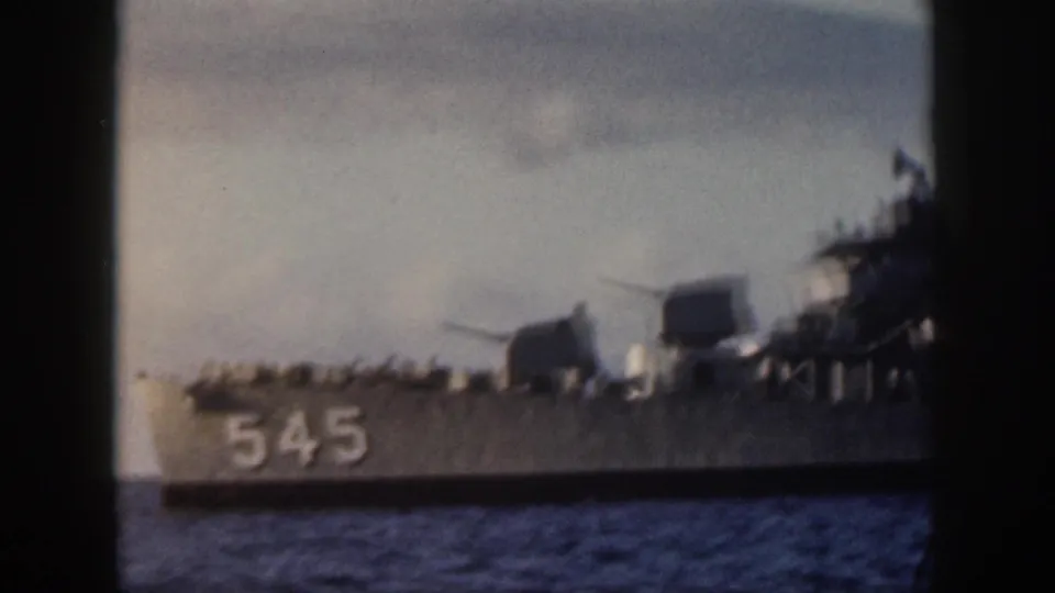 Gray U.S. Navy warship near Oahu with hull number 545 visible, showing gun mounts and deck railings against a cloudy sky.