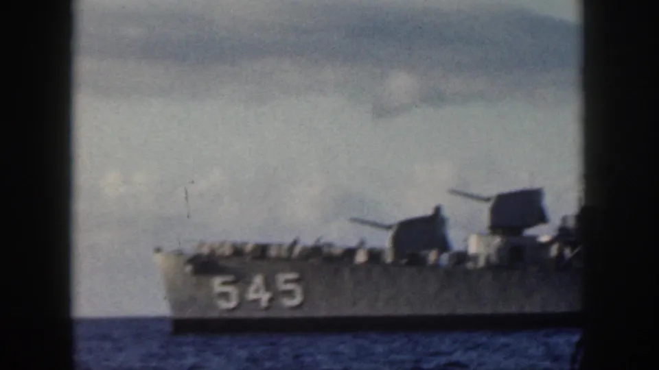 1959 Oahu home-movie view of a gray naval vessel, with hull number 545, forward gun mounts, railings, and ocean water visible.