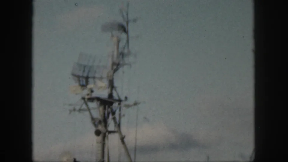 Handheld 1959 Hawaii frame with a blurred naval radar mast and antennas visible through 8mm film grain.