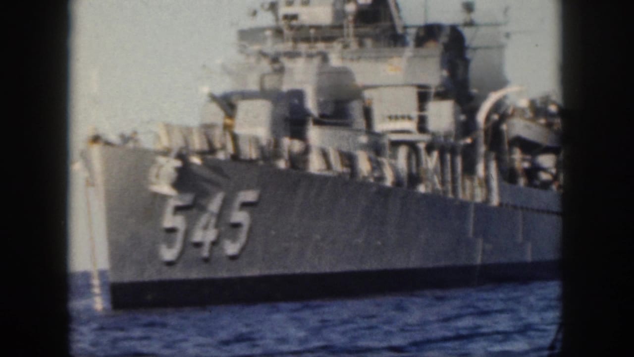 1959 Oahu home-movie frame showing the side of a gray U.S. Navy destroyer with hull number 545, superstructure and deck fittings visible above the waterline.