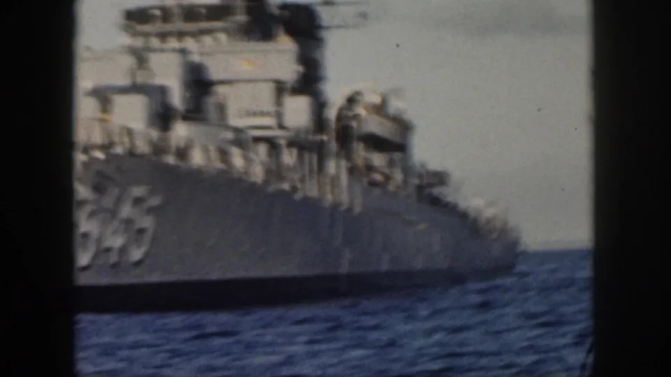 1959 Hawaii home-movie still showing the side of U.S. Navy destroyer 545, including gray hull plating, deck railings, equipment and surrounding sea.