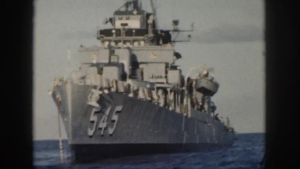 1959 Oahu home-movie frame showing a gray U.S. Navy ship marked 545 approaching across open water.