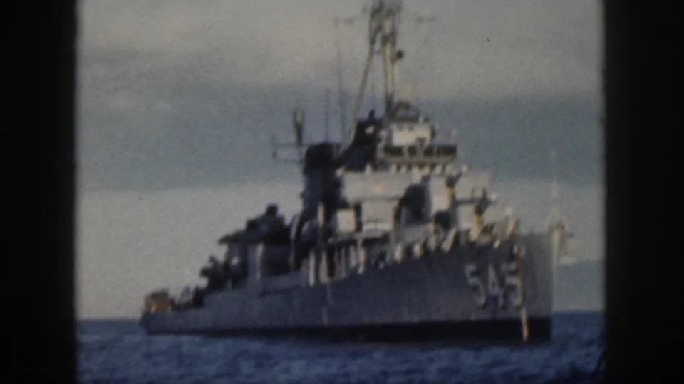 1959 Oahu frame showing a U.S. Navy destroyer marked 545 at sea, with deck structures, mast, and cloudy horizon in a grainy 8mm scan.