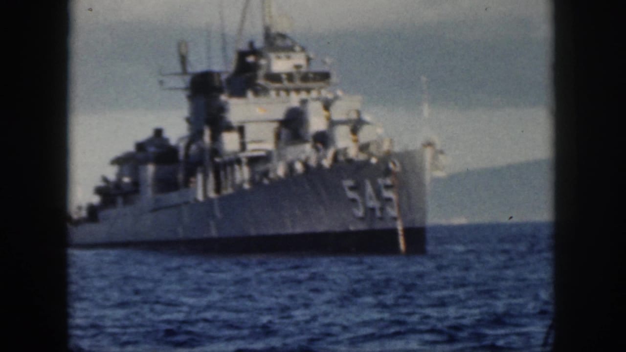 1959 Oahu home-movie frame showing a gray U.S. Navy ship marked 545 on blue water, with dark 8mm frame edges.