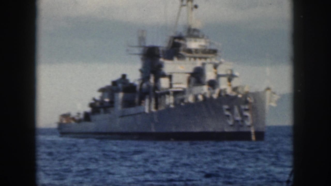 Navy ship marked 545 seen farther right on the water with hills in the distance.