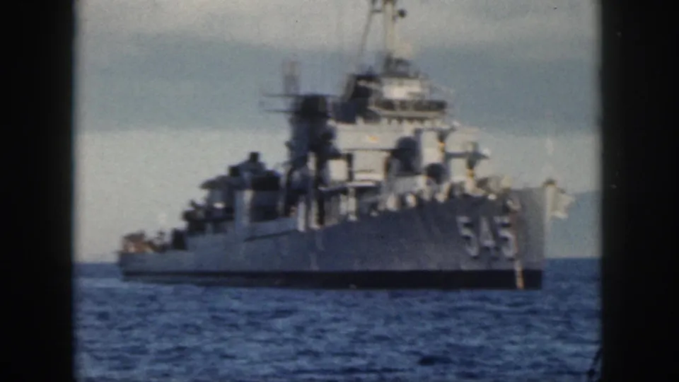 1959 Oahu frame of a gray Navy vessel marked 545 on the ocean, with a faint mountainous shoreline behind it.