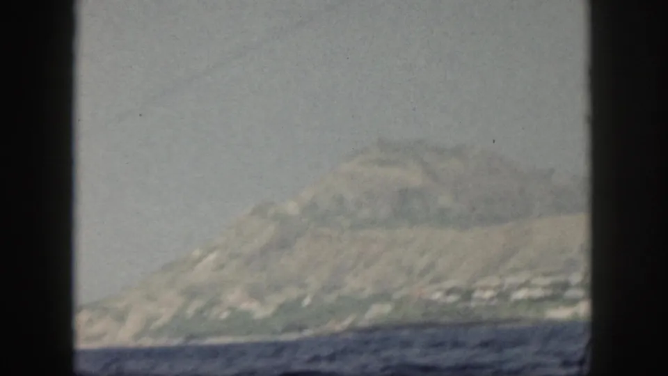 1959 Oahu home-movie view of a mountainous coastline across the water, filmed through soft haze and faded 8mm color.