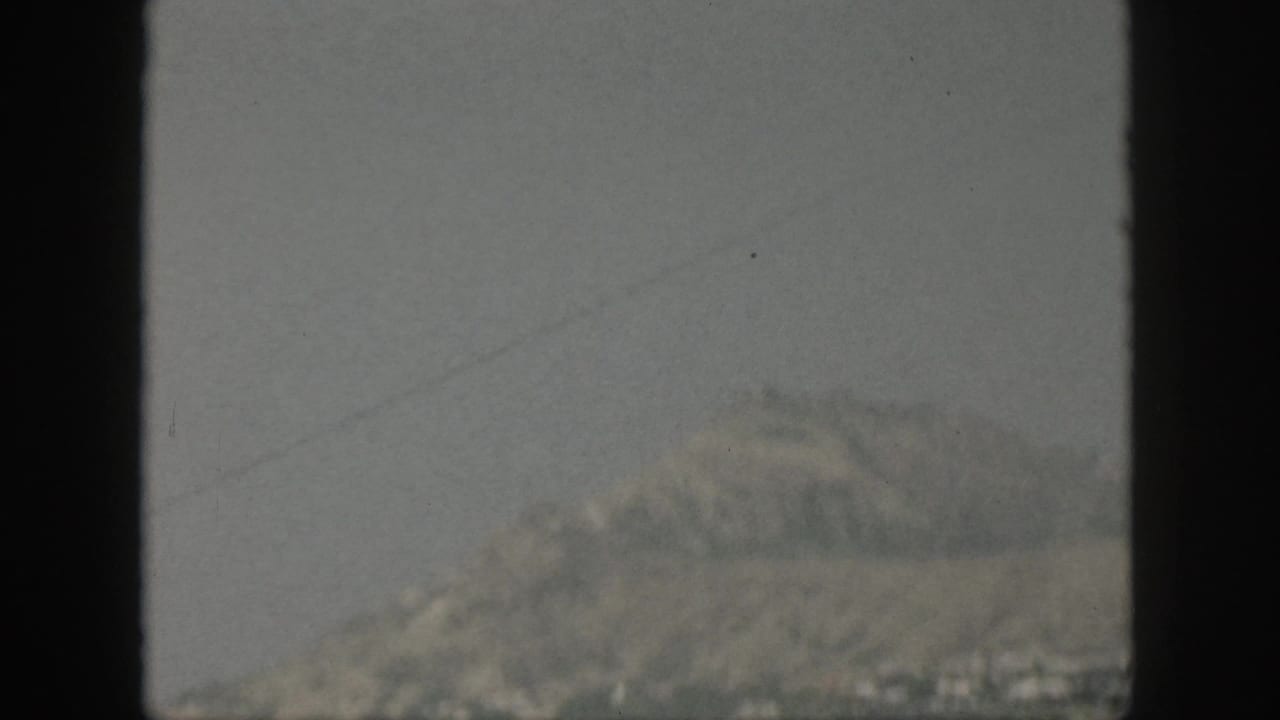 1959 Oahu coastline appears in haze beyond the ocean, framed by dark vertical bars from a boat window.