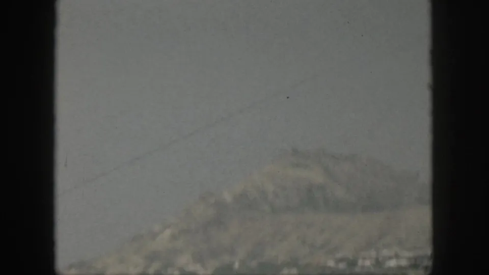 1959 Oahu coastline appears in haze beyond the ocean, framed by dark vertical bars from a boat window.