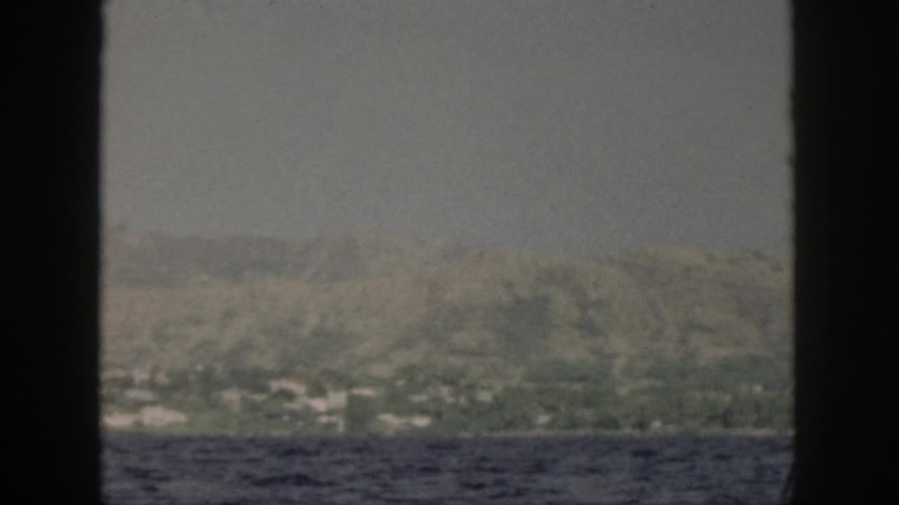 Coastline and hills seen across blue ocean through dark boat-window dividers.