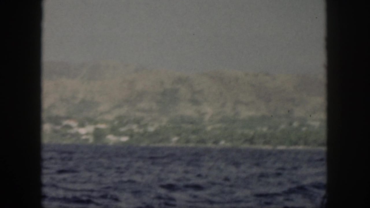 Distant mountain ridge and shoreline beyond choppy ocean, framed by boat windows.