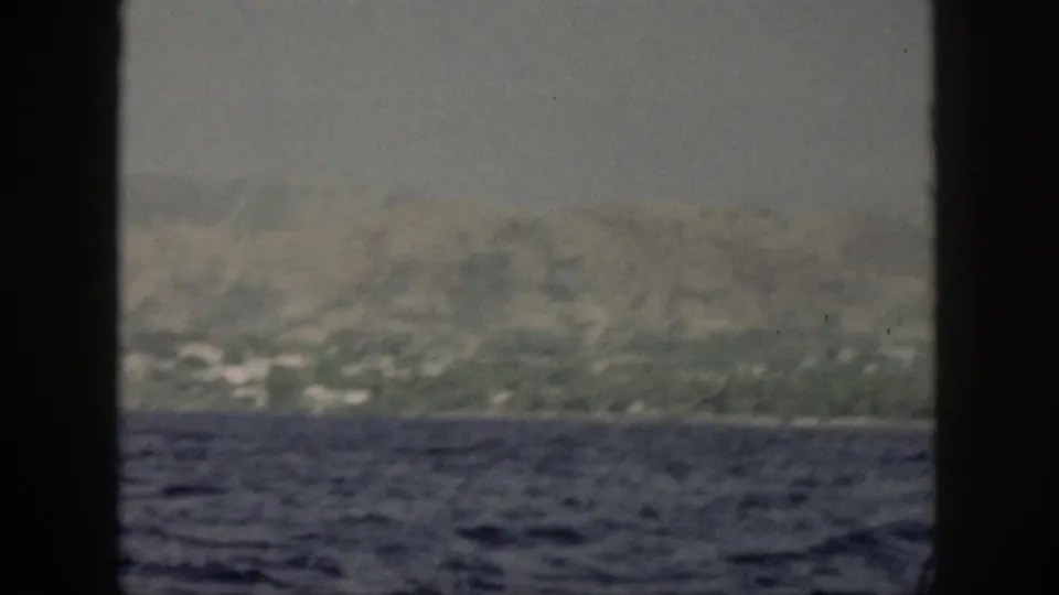 1959 Oahu coast and mountain ridge seen from offshore, with blue water below and dark vertical window bars in the frame.