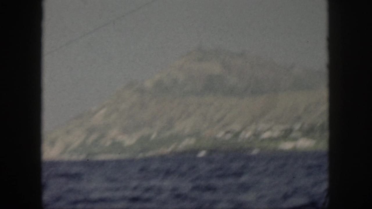 Mountainous island coastline and dark water partly divided by a central black frame bar.