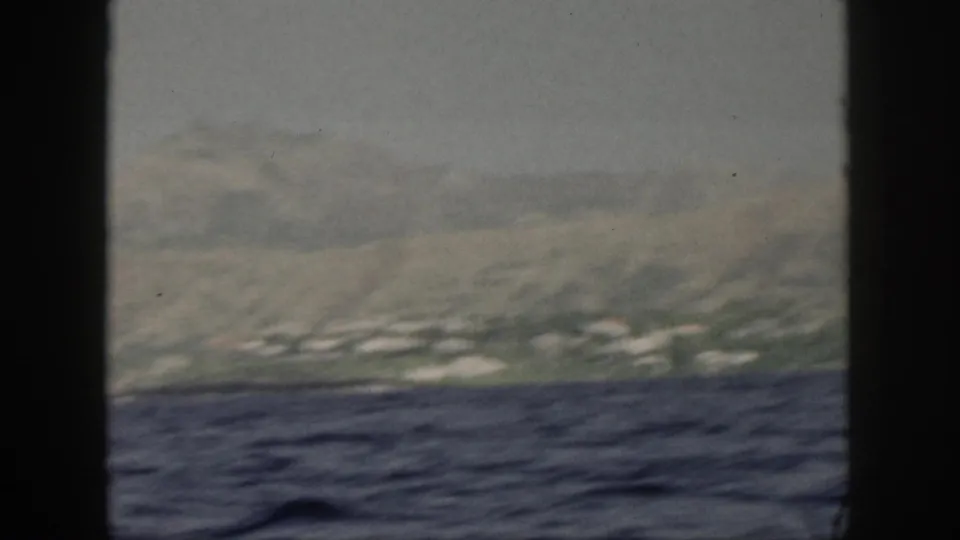 End frame from a 1959 Oahu boat-view clip, showing choppy ocean, a distant shoreline, and soft mountain slopes under haze.
