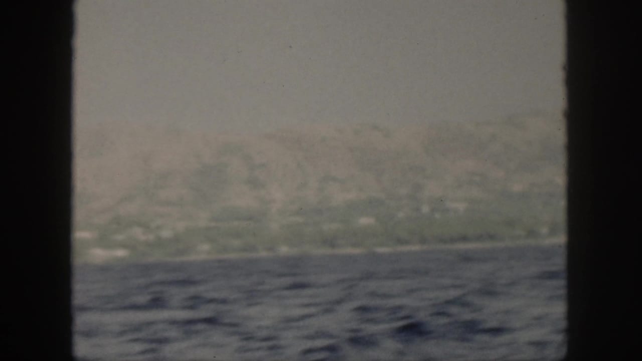 Blue water and hazy island hills framed by dark vertical window bars.