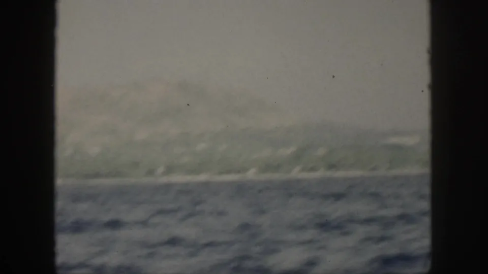 The final frame keeps the 1959 Oahu coastline in view, with hazy hills, a thin shore, and textured blue water between window bars.