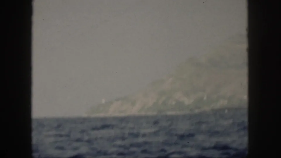 1959 Oahu coastal view with a mountain slope and shoreline across blue water, partially obscured by a dark window or frame edge.