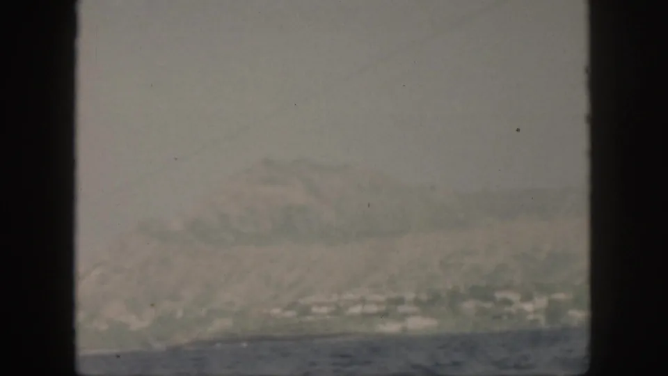 1959 Oahu 8mm view from a boat toward fog-covered hills and small pale buildings along the shoreline.