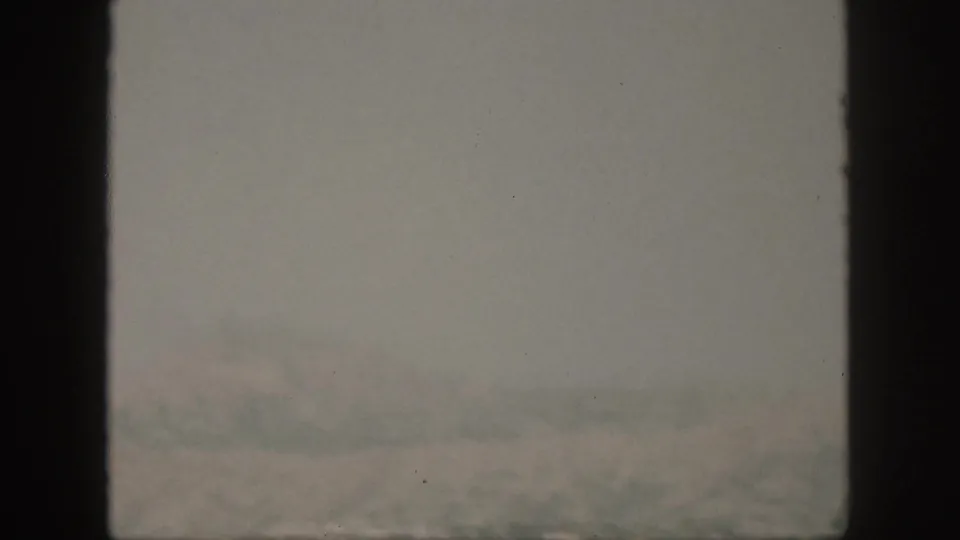 A soft 1959 Oahu boat-view frame with fog, pale shoreline forms, and choppy water under muted 8mm color.
