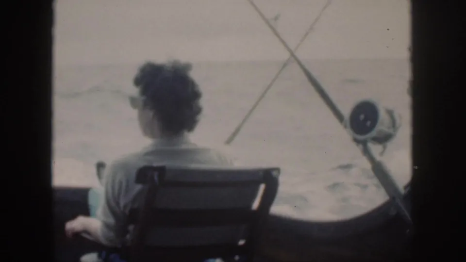 The man turns slightly in his chair on the boat, with rods and reel beside him in the Oahu home-movie footage.