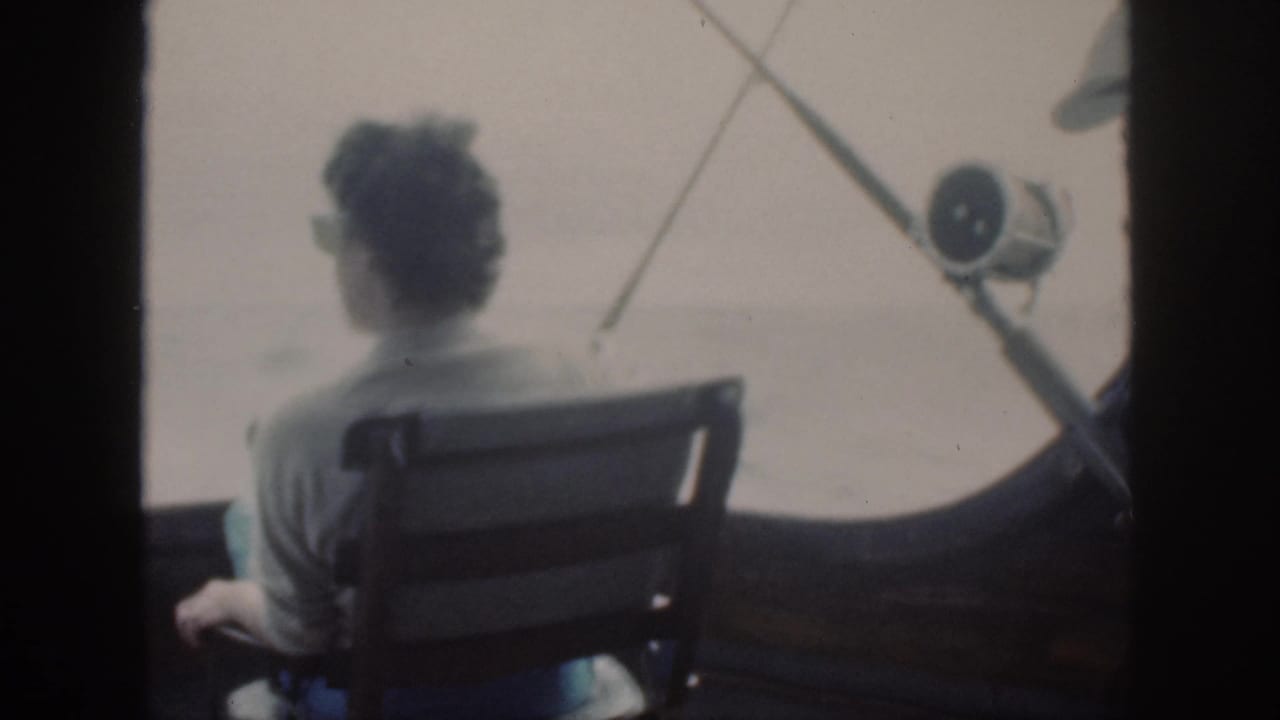 1959 Oahu 8mm frame of a woman seated from behind on a fishing boat, looking toward open water through a dark boat frame.
