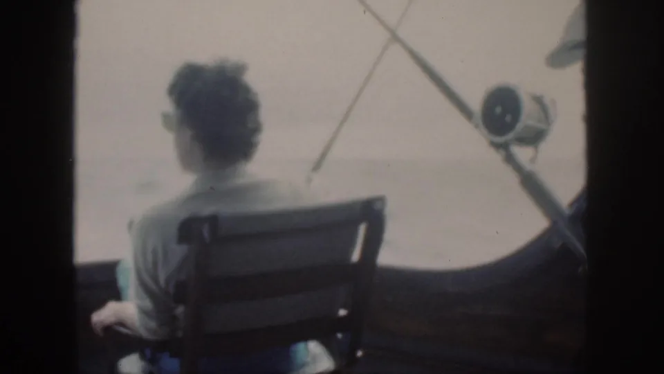 1959 Oahu 8mm frame of a woman seated from behind on a fishing boat, looking toward open water through a dark boat frame.