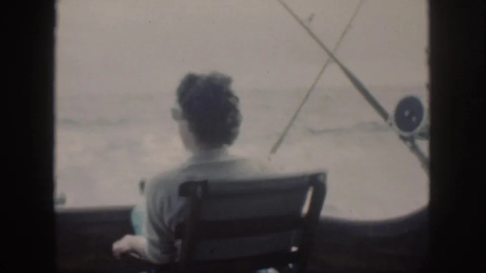 Soft 8mm view from an Oahu fishing boat in 1959, showing a woman seated quietly while rods cross the ocean backdrop.