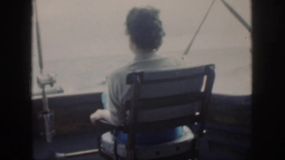 1959 Oahu home-movie frame of a woman seated at the stern or deck area, looking across the sea beside mounted fishing gear.
