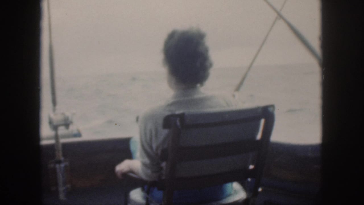 1959 Oahu home-movie frame showing a person seated from behind on a fishing boat, looking toward calm open water.