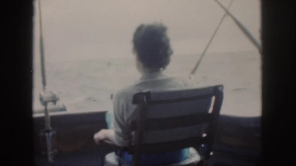 1959 Oahu home-movie frame showing a person seated from behind on a fishing boat, looking toward calm open water.