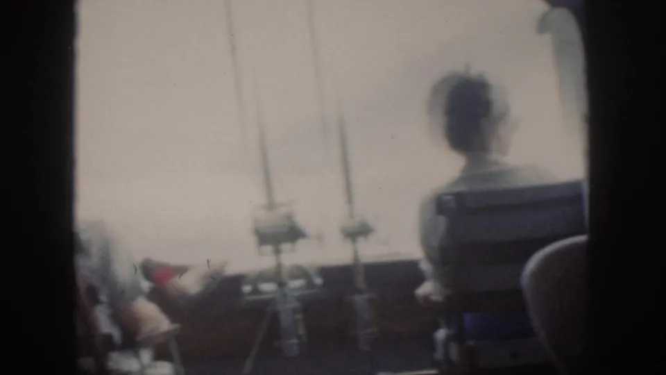 Soft 8mm frame from Oahu in 1959 showing a person seated on a boat deck near fishing rods, with another passenger partly visible.