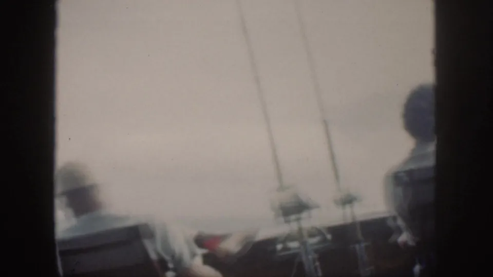 Final 1959 Oahu boat frame with fishing rods, rail hardware, open water, and partly visible seated passengers on deck.