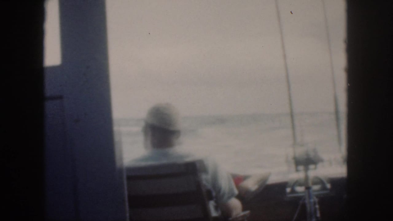 Soft 8mm frame from Oahu in 1959 showing an adult seated near fishing rods while looking out over hazy water.
