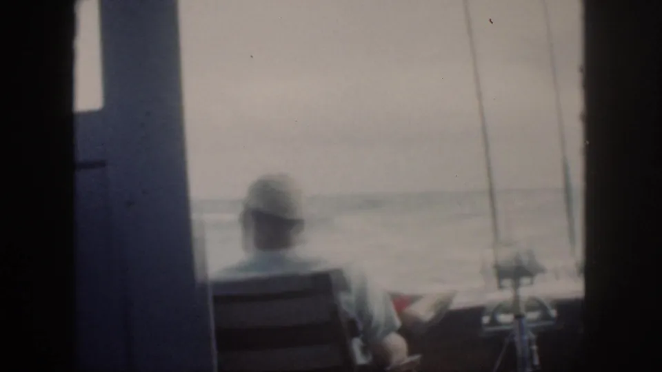 Soft 8mm frame from Oahu in 1959 showing an adult seated near fishing rods while looking out over hazy water.