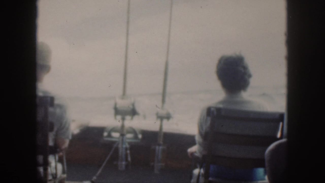 A seated figure faces open water beside mounted fishing rods on a boat.