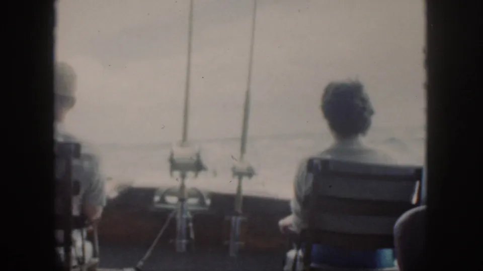 Soft 8mm view from a boat in Oahu, with a seated passenger, fishing rods, and pale sea visible through dark framing.
