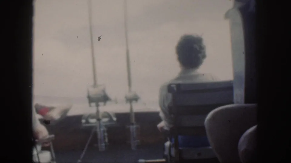 Vintage Oahu boat-ride frame showing a passenger from behind, deck-mounted rods, and bright water beyond the rail.