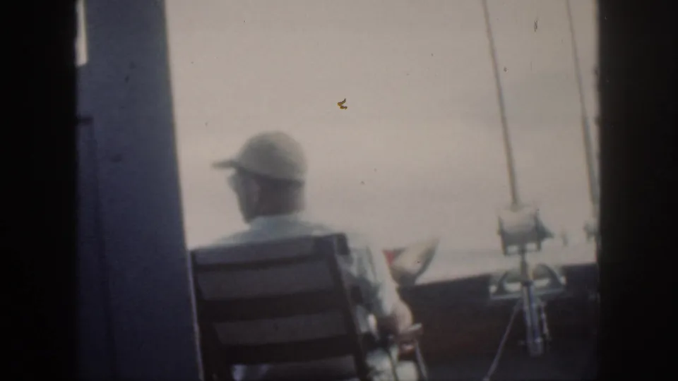 1959 Oahu frame of a capped man seated from behind on a small boat, with fishing rods and hazy open water ahead.
